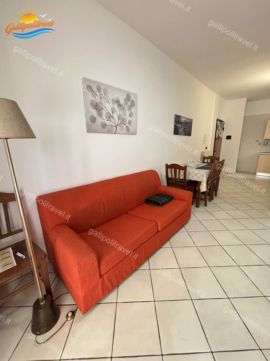 Soggiorno con divano rosso e lampada a piantana del Trilocale B2/3, Residence Rosa Virginia Gallipoli