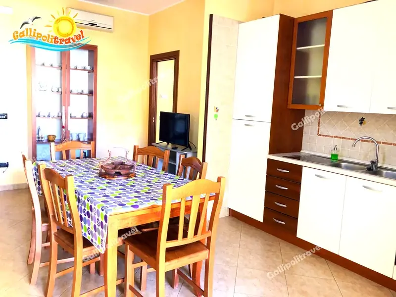 Soggiorno del Trilocale D1/3 con credenza in legno, cucina bianca e TV