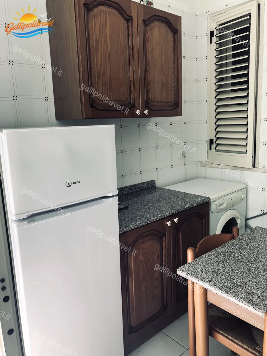Cucina con frigorifero, lavatrice e pensili in legno del Trilocale Tamerici 02, Baia Verde Gallipoli