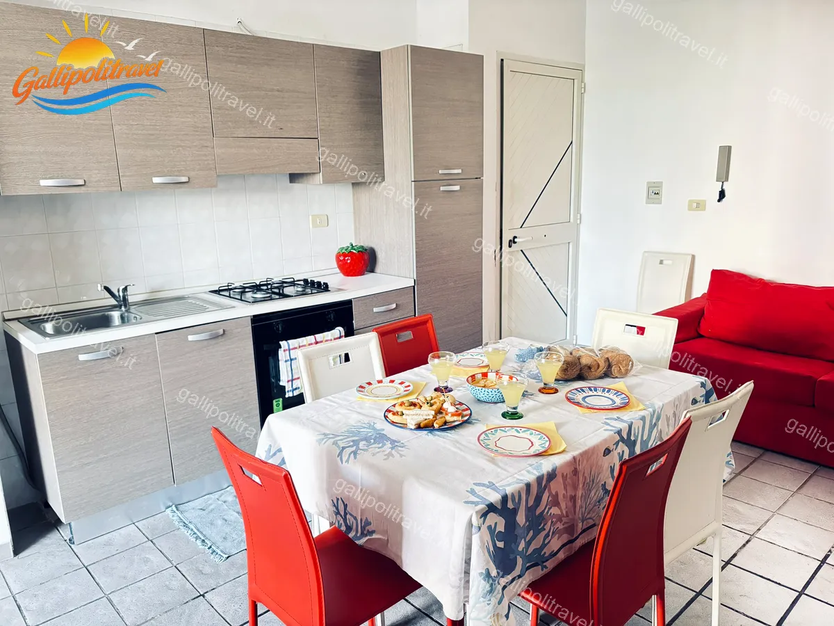 Cucina con tavolo e divano rosso del Trilocale Mimosa, Baia Verde Gallipoli