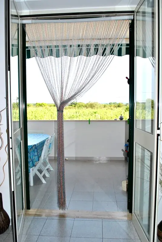 Ingresso sul balcone del Trilocale Girasole con tende a fili e vista sulla vegetazione